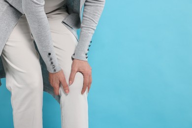 Arthritis symptoms. Woman suffering from pain in knee on light blue background, closeup. Space for text