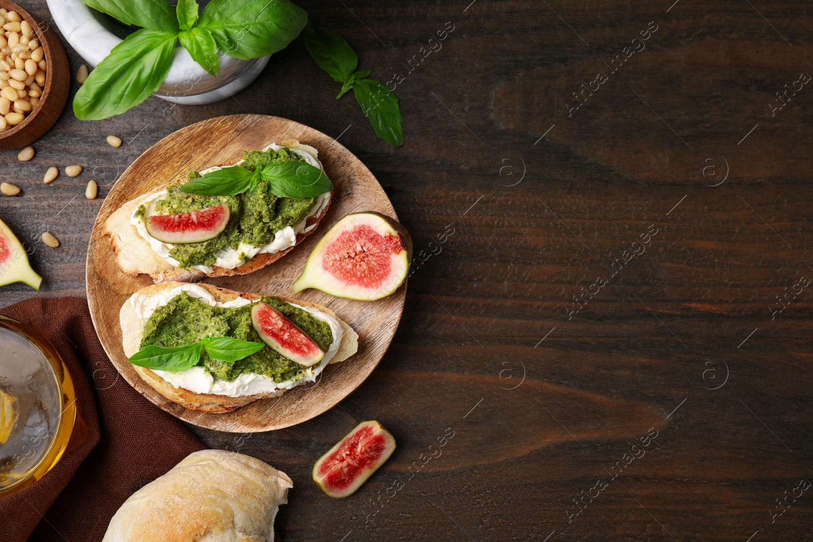 Photo of Tasty bruschettas with cream cheese, pesto sauce, figs and fresh basil on wooden table, flat lay. Space for text