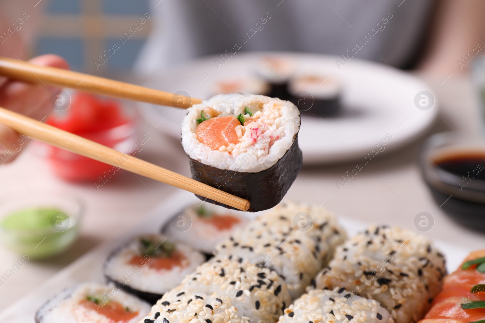 Photo of Woman holding tasty sushi roll with chopsticks at table, closeup