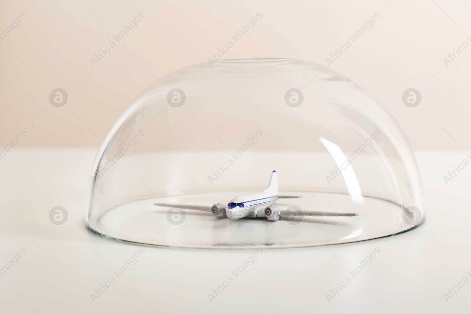 Photo of Toy plane under glass dome on white table. Travel insurance concept