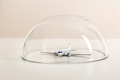 Photo of Toy plane under glass dome on white table. Travel insurance concept