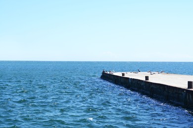 Photo of Beautiful concrete pier in sea on sunny day, space for text