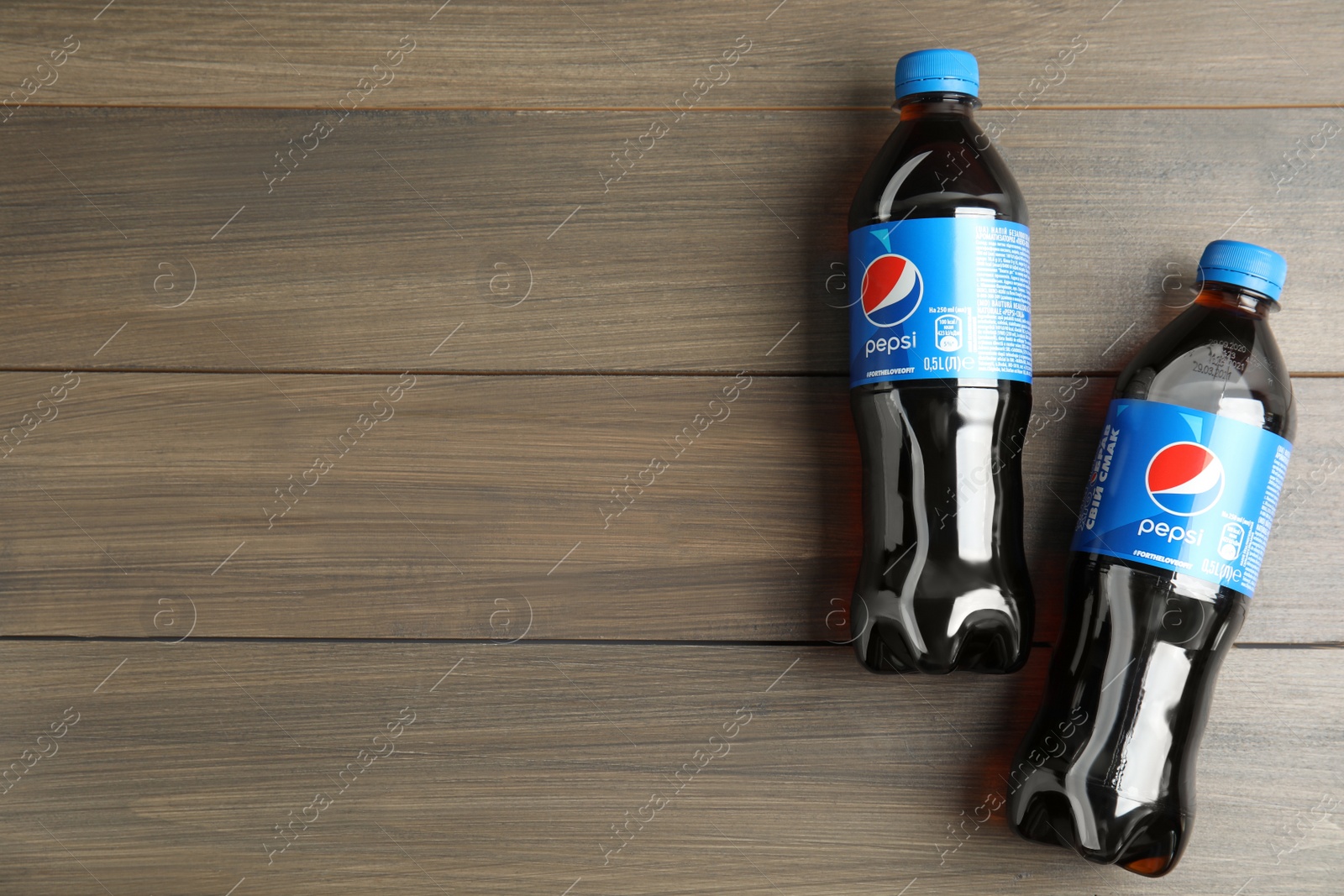 Photo of MYKOLAIV, UKRAINE - FEBRUARY 9, 2021: Bottles of Pepsi on wooden table, flat lay. Space for text