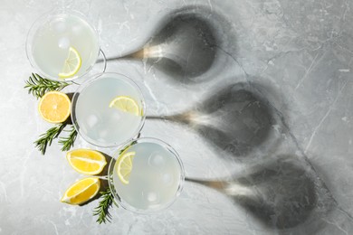 Photo of Martini glasses of refreshing cocktail decorated with lemon slices and rosemary on light grey textured table, flat lay. Space for text