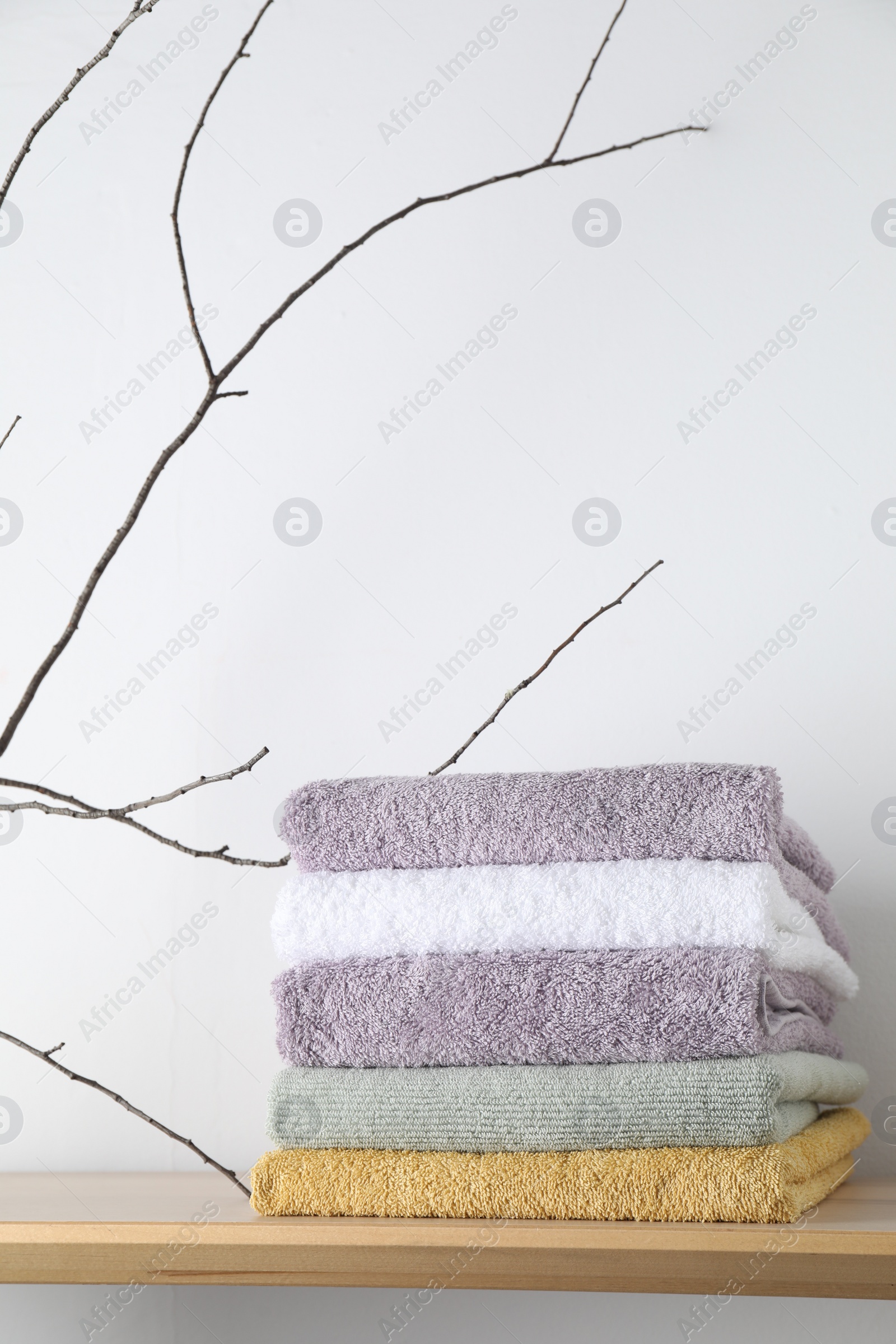 Photo of Stacked terry towels and tree branch on wooden shelf near white wall