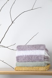 Photo of Stacked terry towels and tree branch on wooden shelf near white wall