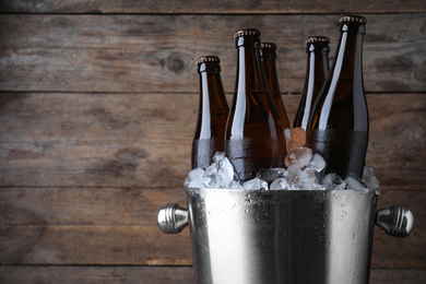 Photo of Metal bucket with beer and ice cubes on wooden background, closeup. Space for text