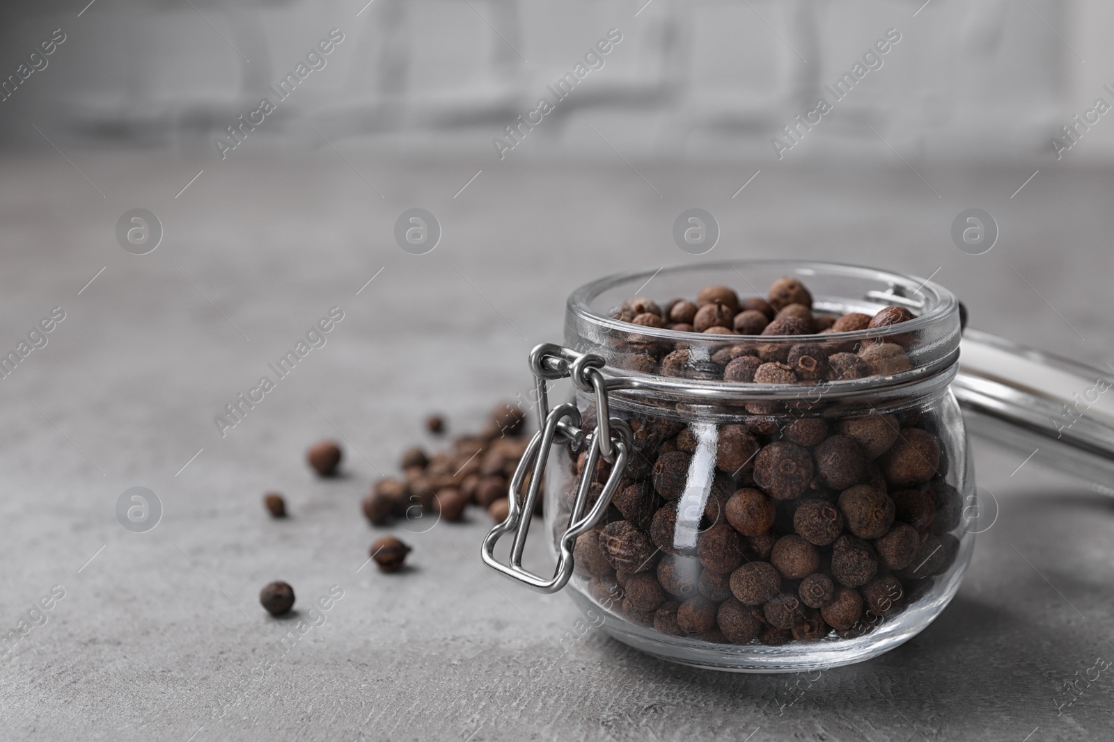 Photo of Black peppercorns in jar on grey table, closeup. Space for text