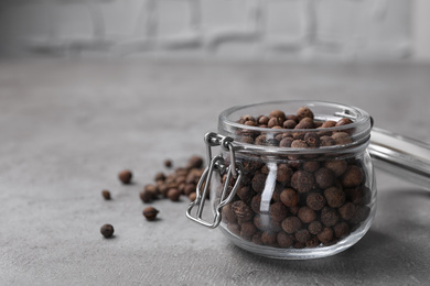 Black peppercorns in jar on grey table, closeup. Space for text