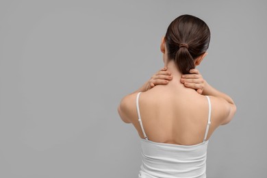 Woman touching her neck on grey background, back view. Space for text