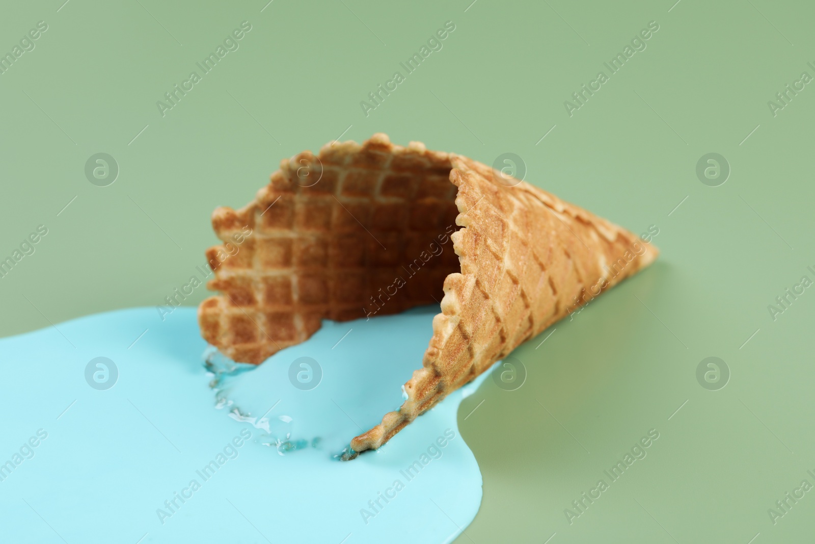 Photo of Melted ice cream and wafer cone on green background, closeup