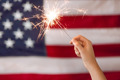 Photo of Woman holding bright burning sparkler against American flag, closeup