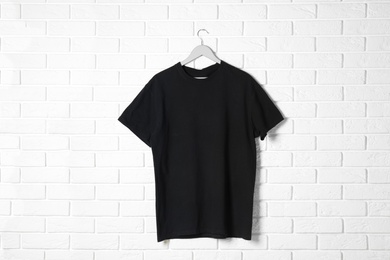 Photo of Hanger with black t-shirt against brick wall. Mockup for design