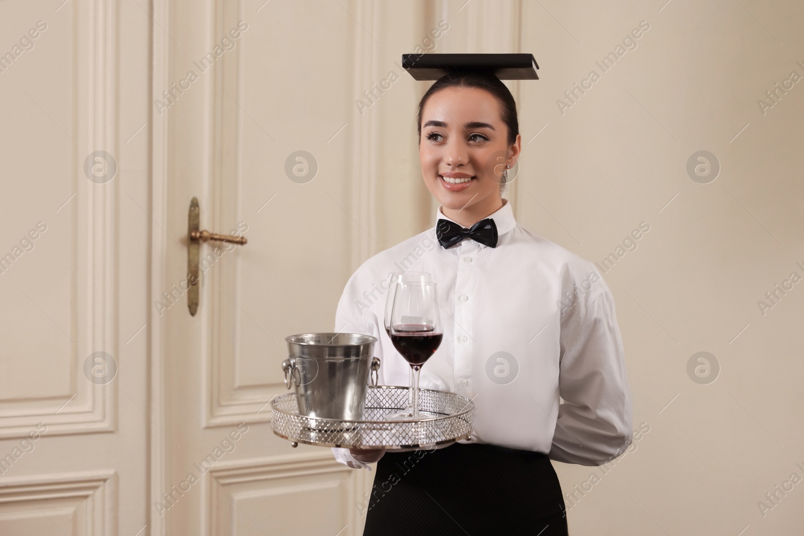 Photo of Woman with tray and book on head practicing good posture indoors, space for text. Professional butler courses