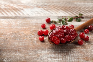 Tasty dried cranberries in spoon and fresh ones on rustic wooden table. Space for text