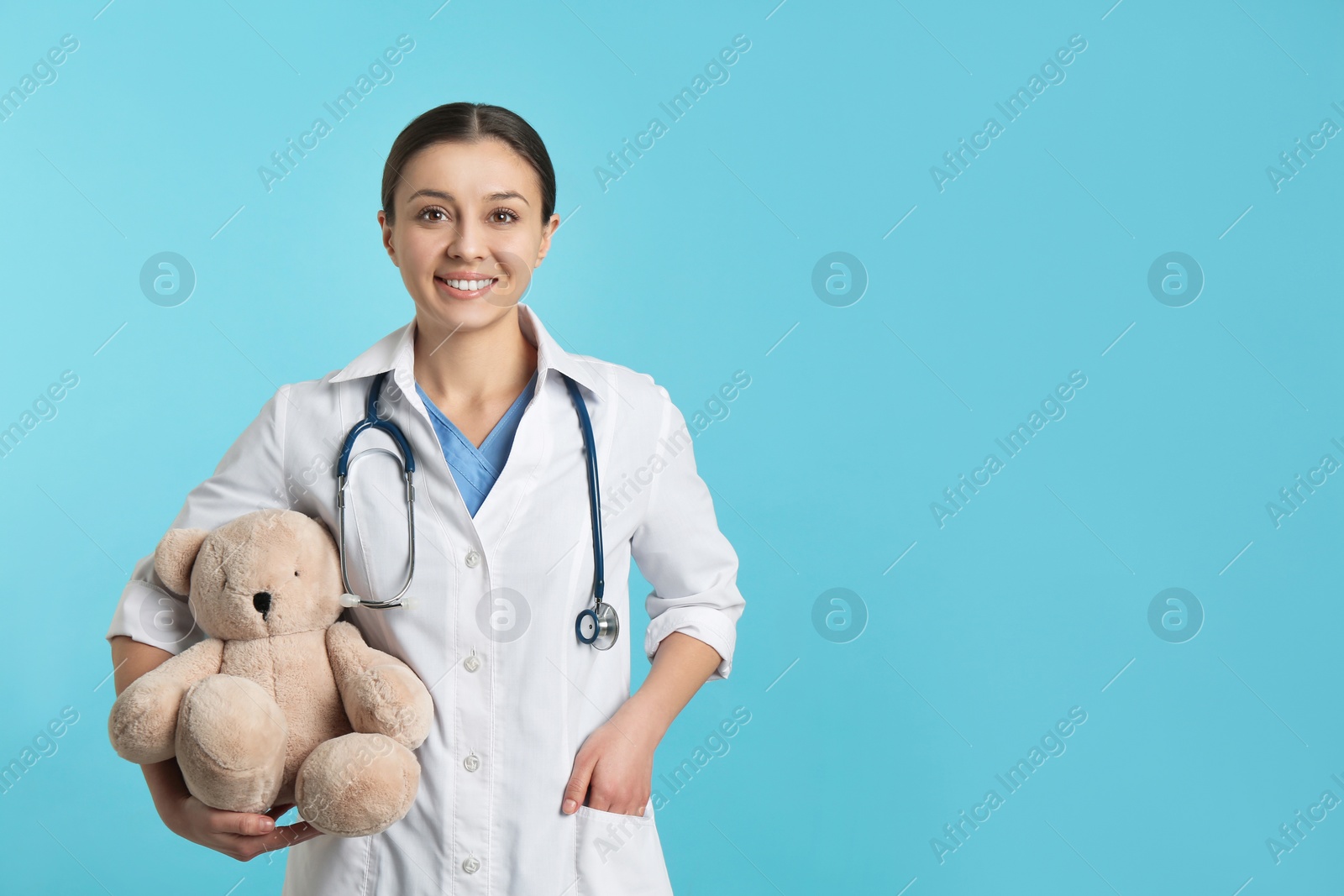 Photo of Pediatrician with teddy bear and stethoscope on turquoise background, space for text