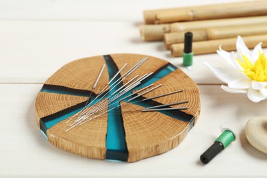 Wooden coaster with acupuncture needles on white table, closeup