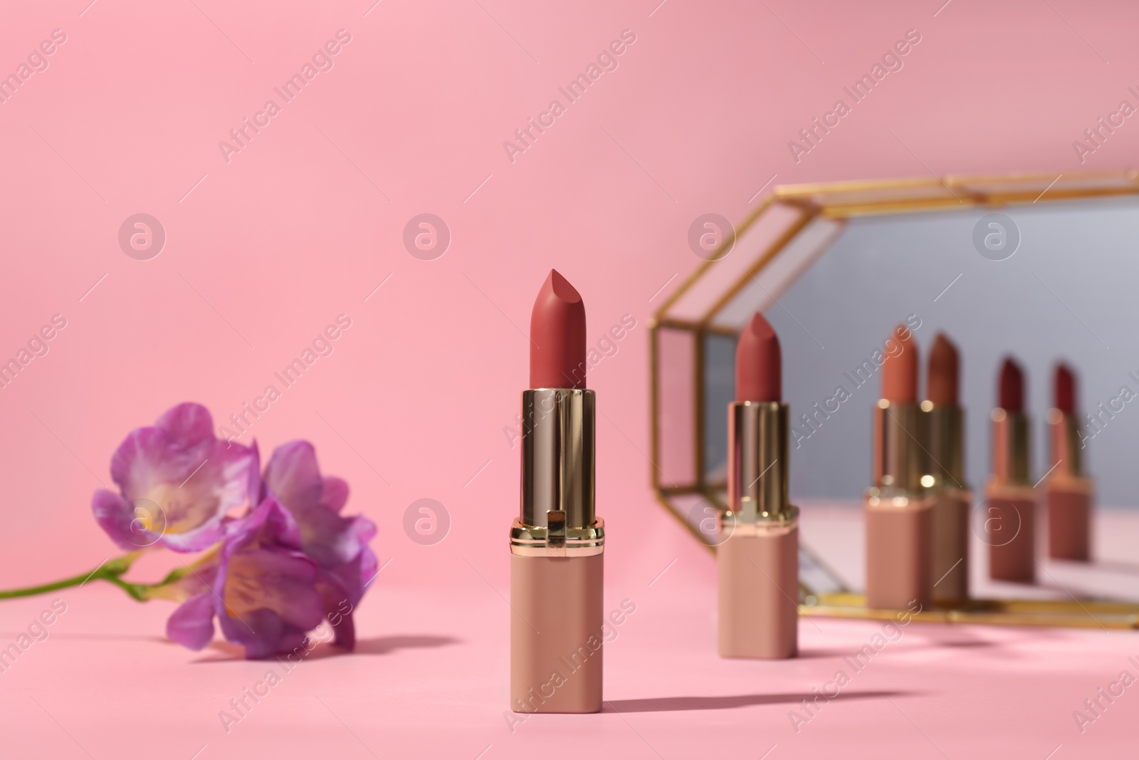 Photo of Different lipsticks and flower near mirror on pink background