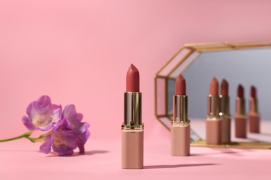 Different lipsticks and flower near mirror on pink background