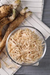 Photo of Grated horseradish and roots on grey wooden table, flat lay