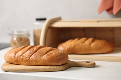 Photo of Wooden bread basket with freshly baked loaves on white marble table in kitchen