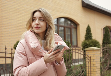 Young woman using mobile phone outdoors. Space for text