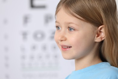 Photo of Cute little girl against vision test chart, closeup