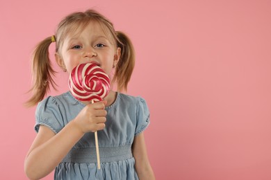 Photo of Portrait of cute girl licking lollipop on pink background, space for text