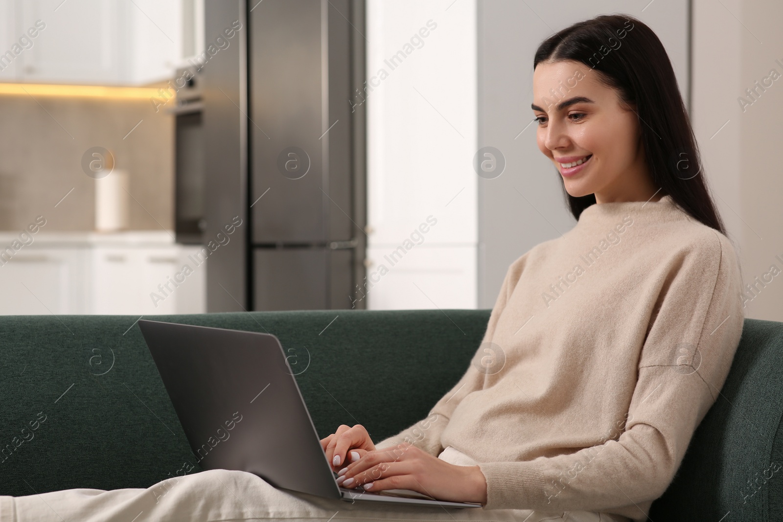 Photo of Happy woman working with laptop on sofa in kitchen