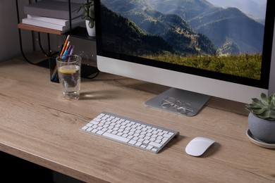 Photo of Modern computer and glass of lemon water on wooden table indoors