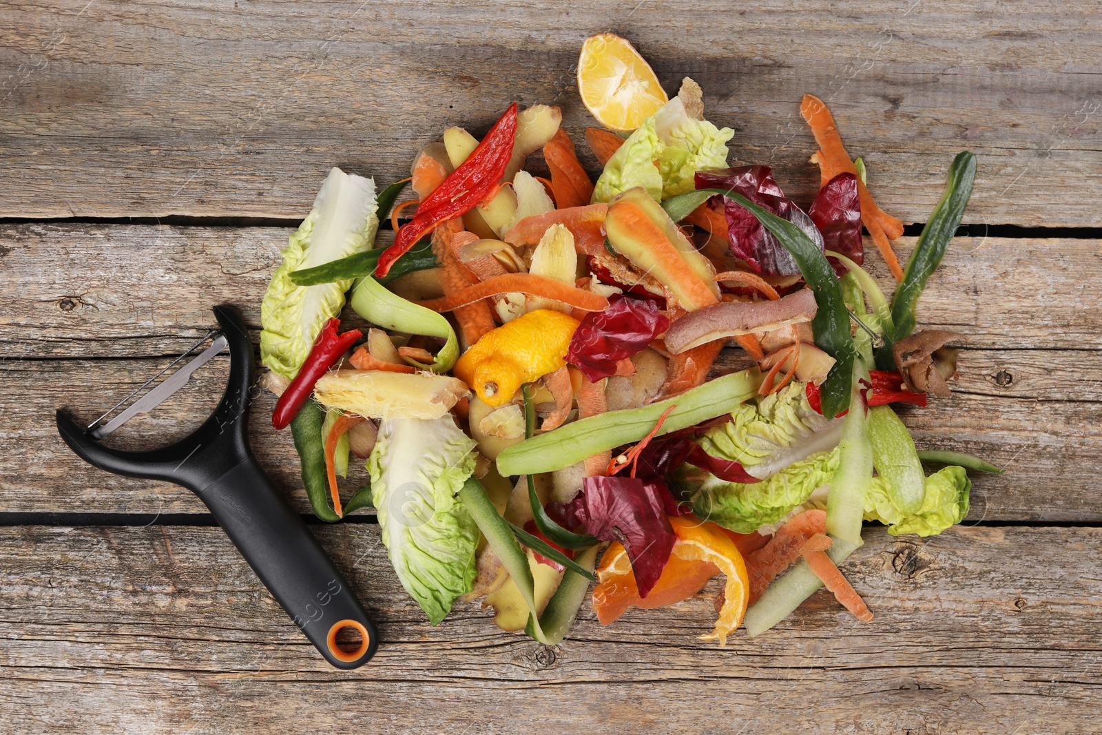 Photo of Peels of fresh vegetables and peeler on wooden table, top view