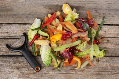 Photo of Peels of fresh vegetables and peeler on wooden table, top view