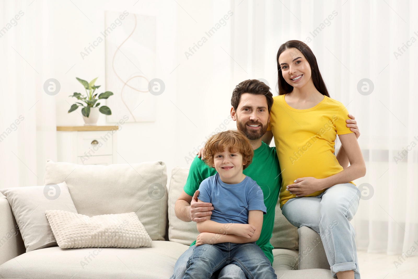 Photo of Family portrait of pregnant mother, father and son in house. Space for text