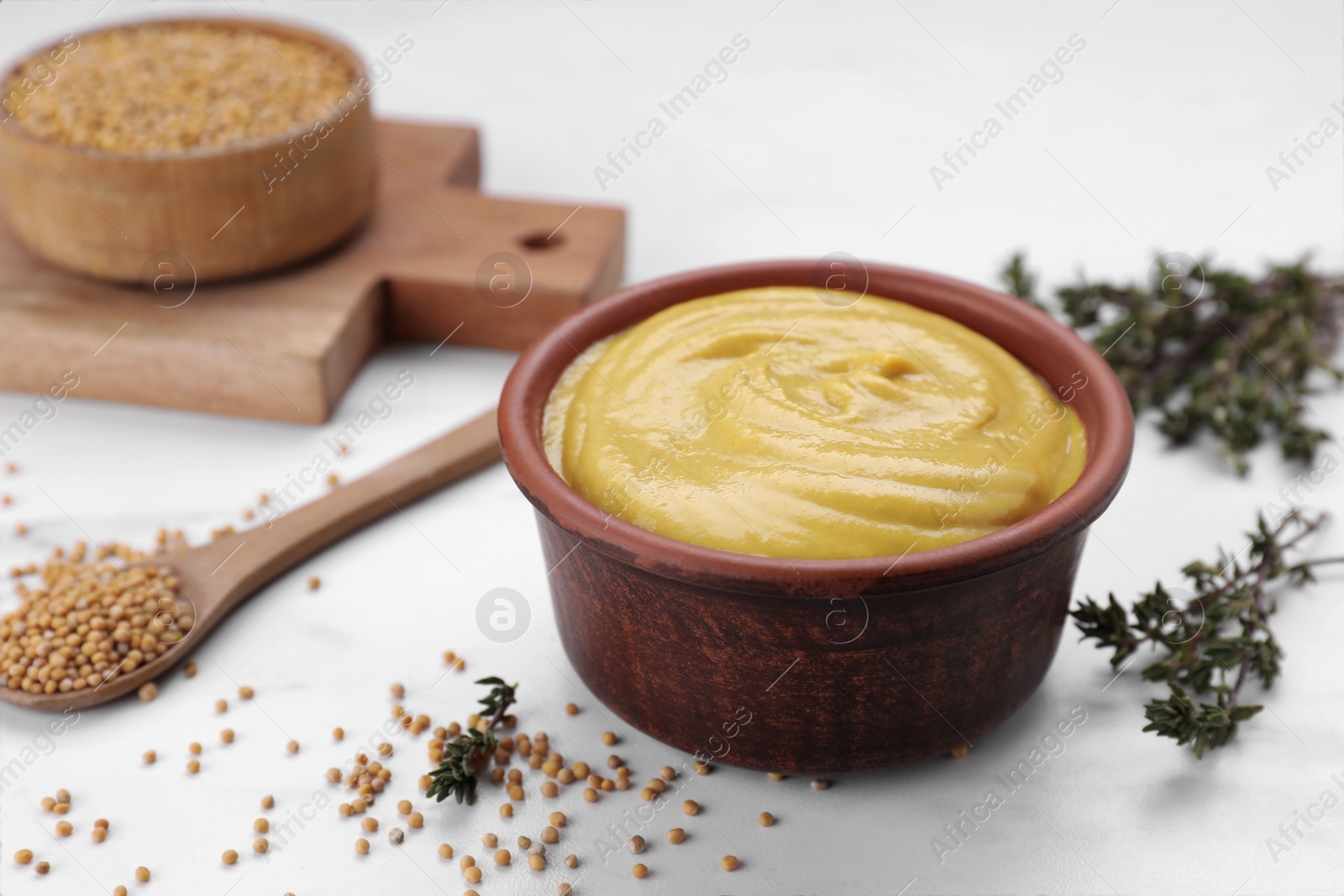 Photo of Bowl with delicious mustard, seeds and dry thyme on white table, closeup