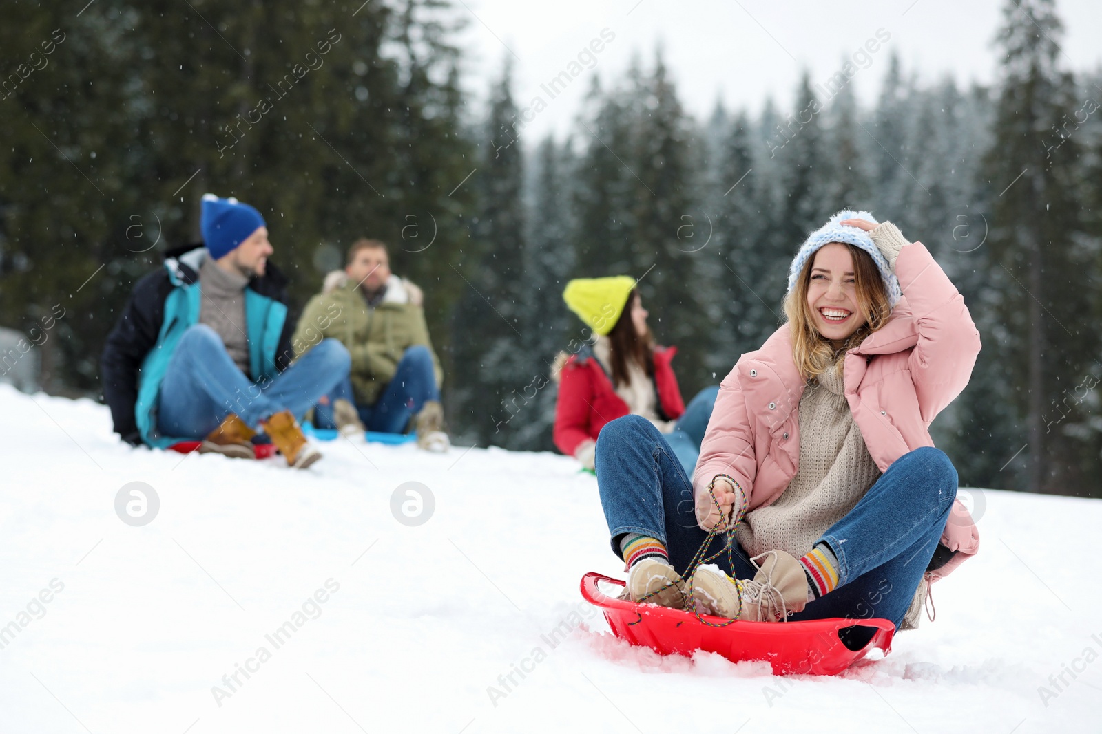 Photo of Happy friends sliding on sleds outdoors. Winter vacation