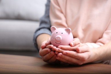 Photo of Couple with piggy bank at wooden table, closeup