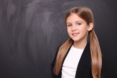 Photo of Smiling schoolgirl near blackboard. Space for text