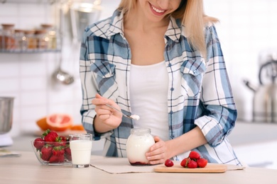 Photo of Young attractive woman eating tasty yogurt at table in kitchen