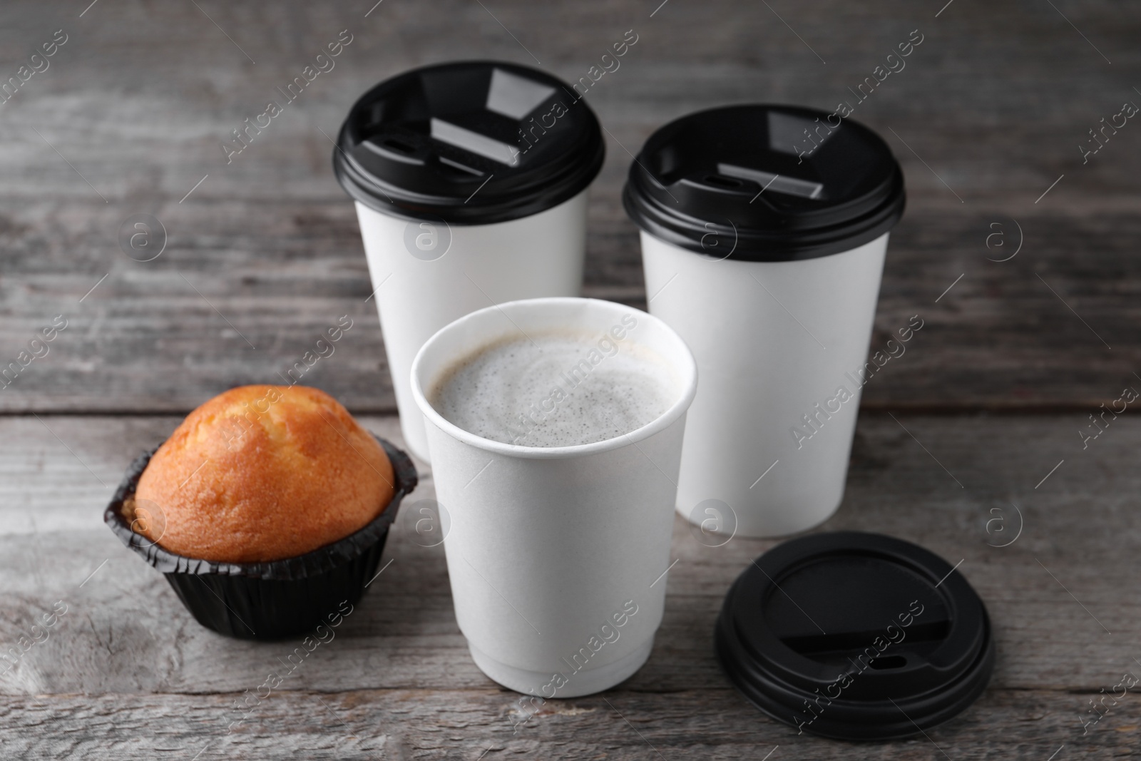 Photo of Coffee to go. Paper cups with tasty drink and muffin on wooden table