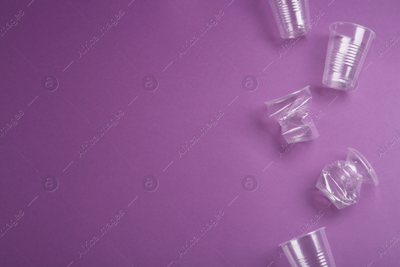 Photo of Plastic cups on purple background, flat lay. Space for text