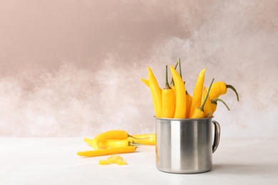 Metal mug with ripe chili peppers on table