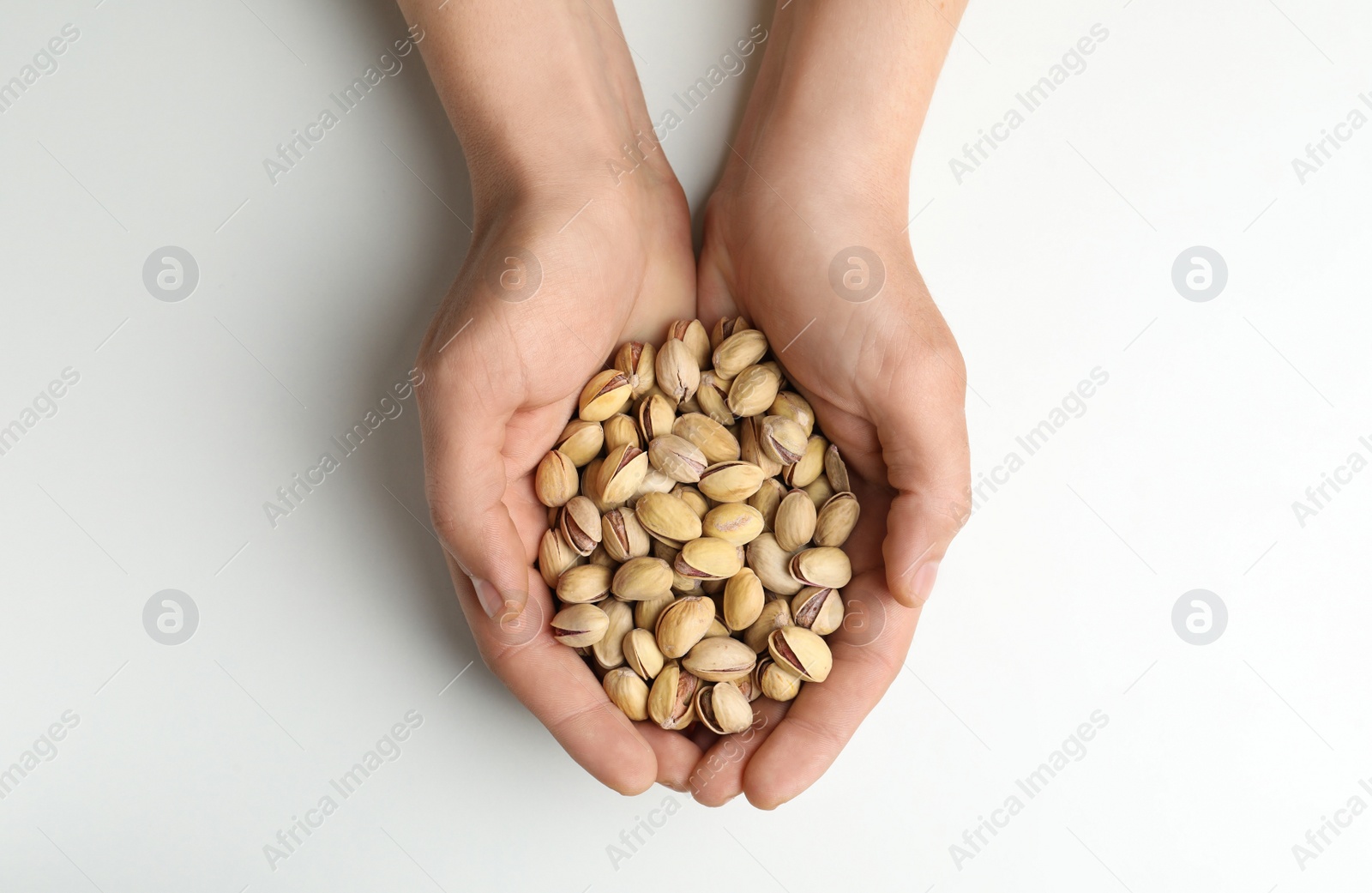 Photo of Woman holding tasty roasted pistachio nuts on white background, top view