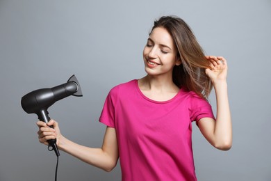 Photo of Beautiful young woman using hair dryer on grey background