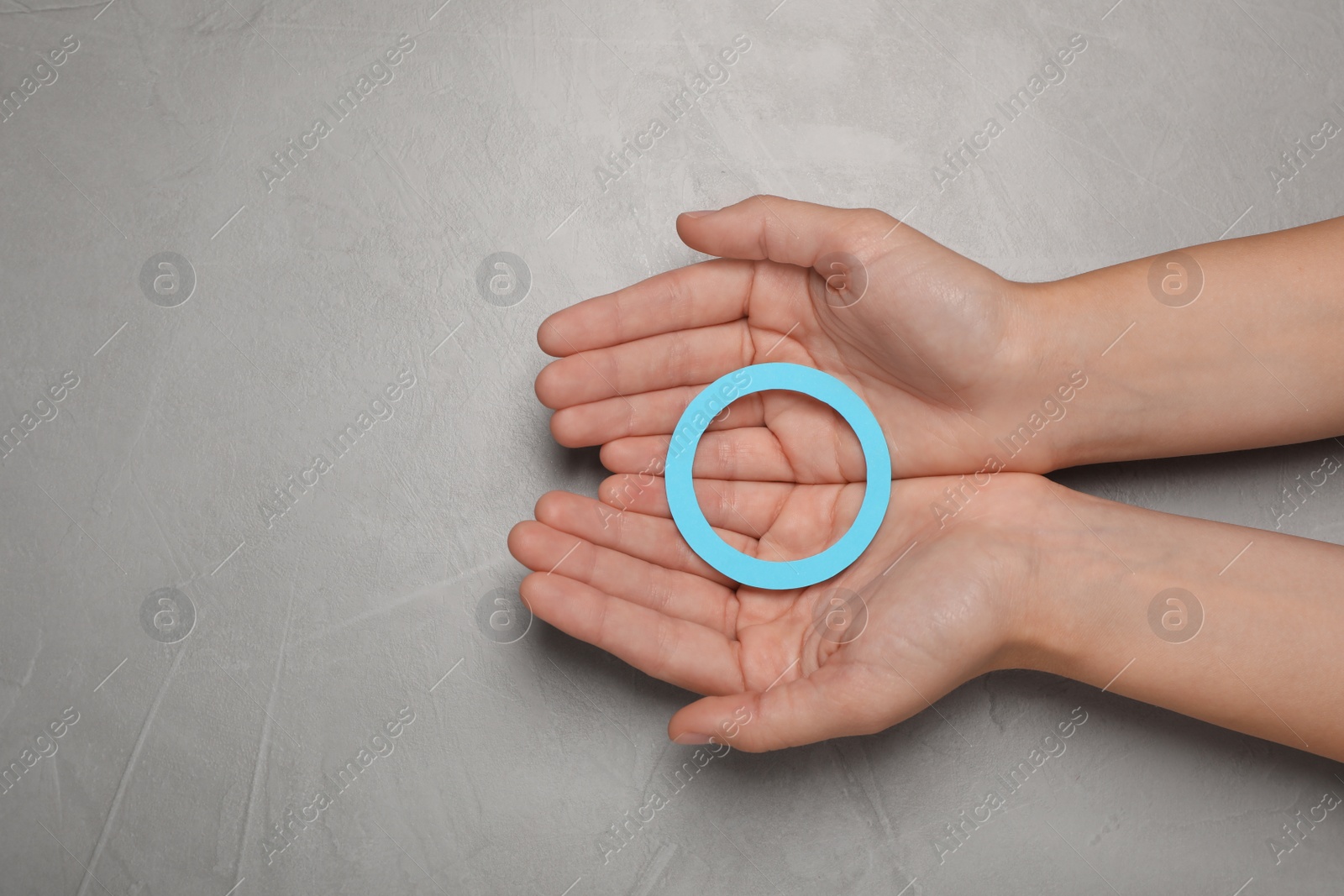 Photo of Woman holding blue paper circle as World Diabetes Day symbol at grey table, top view with space for text