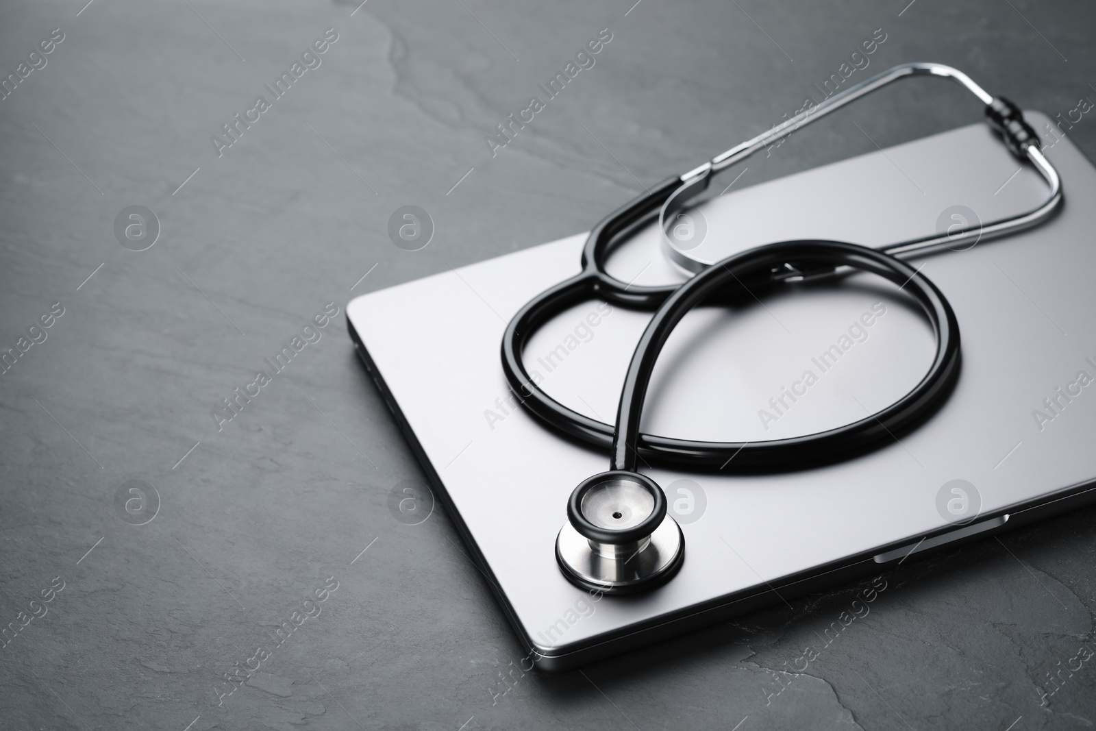 Photo of Modern laptop and stethoscope on black table. Space for text