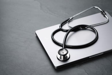 Photo of Modern laptop and stethoscope on black table. Space for text