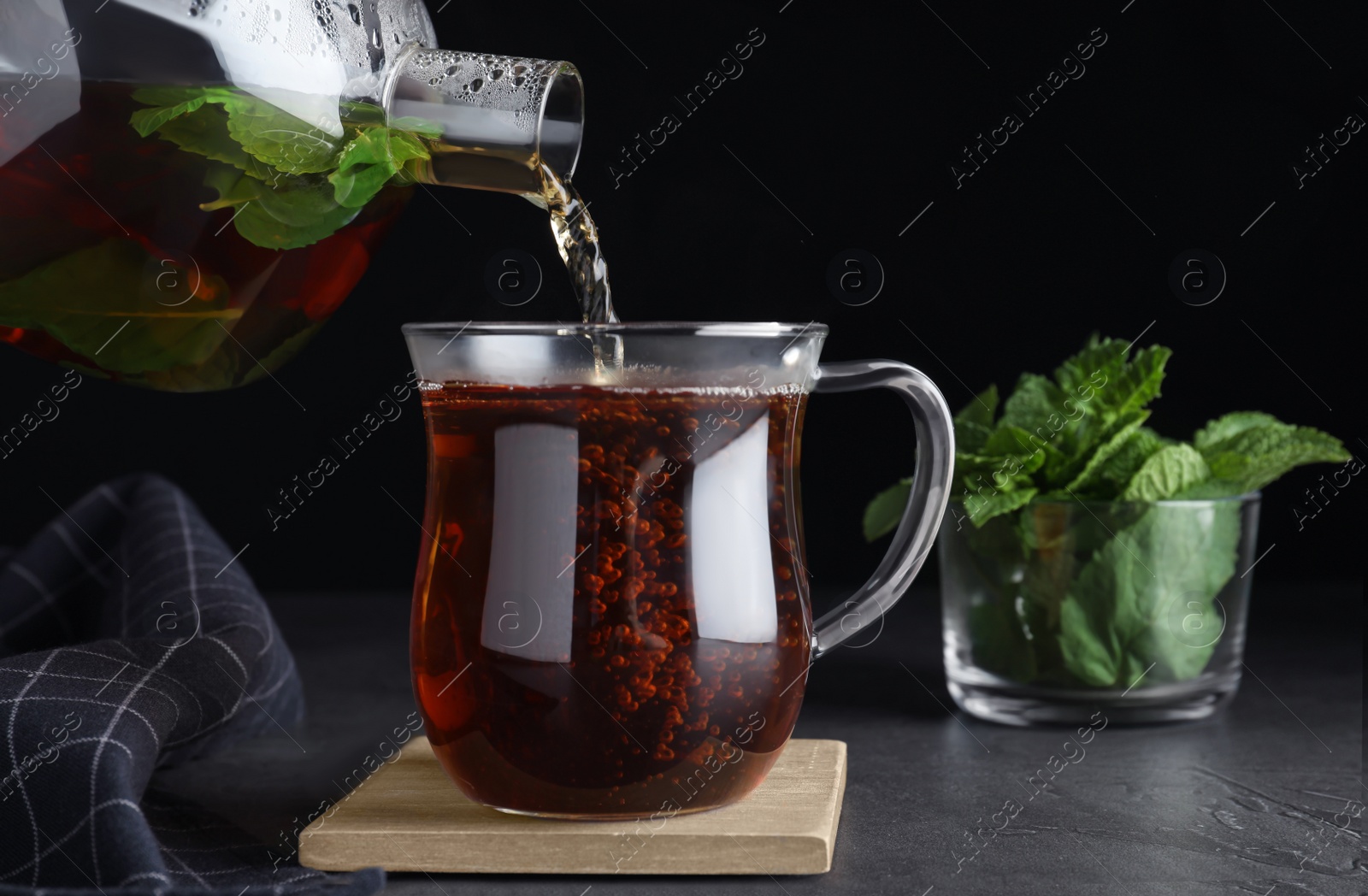 Photo of Pouring fresh mint tea into cup on grey table, closeup