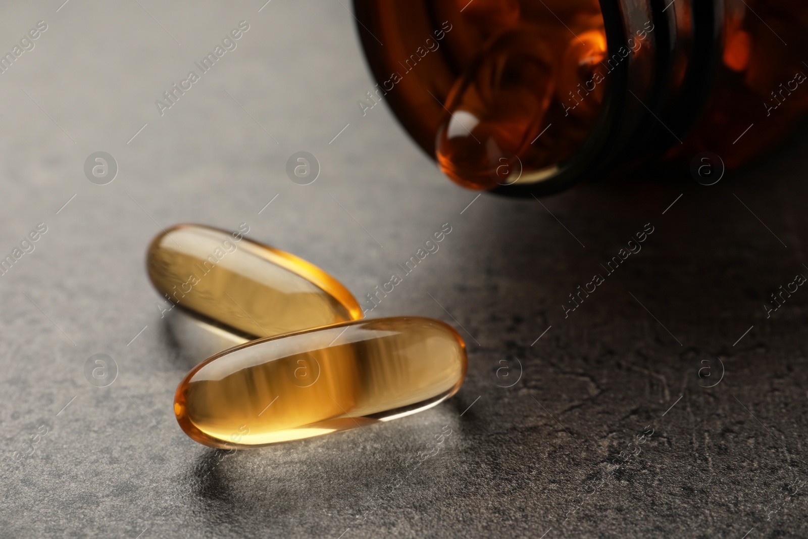 Photo of Overturned bottle with dietary supplement capsules on grey table, closeup