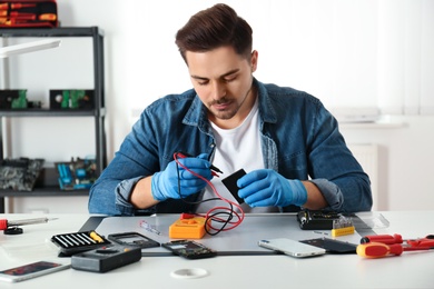 Photo of Technician checking broken smartphone at table in repair shop