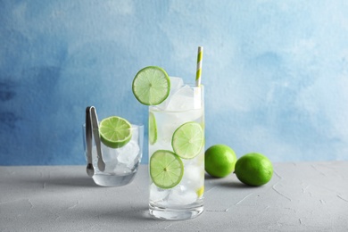 Photo of Glass of drink with lime and ice cubes on table against color background